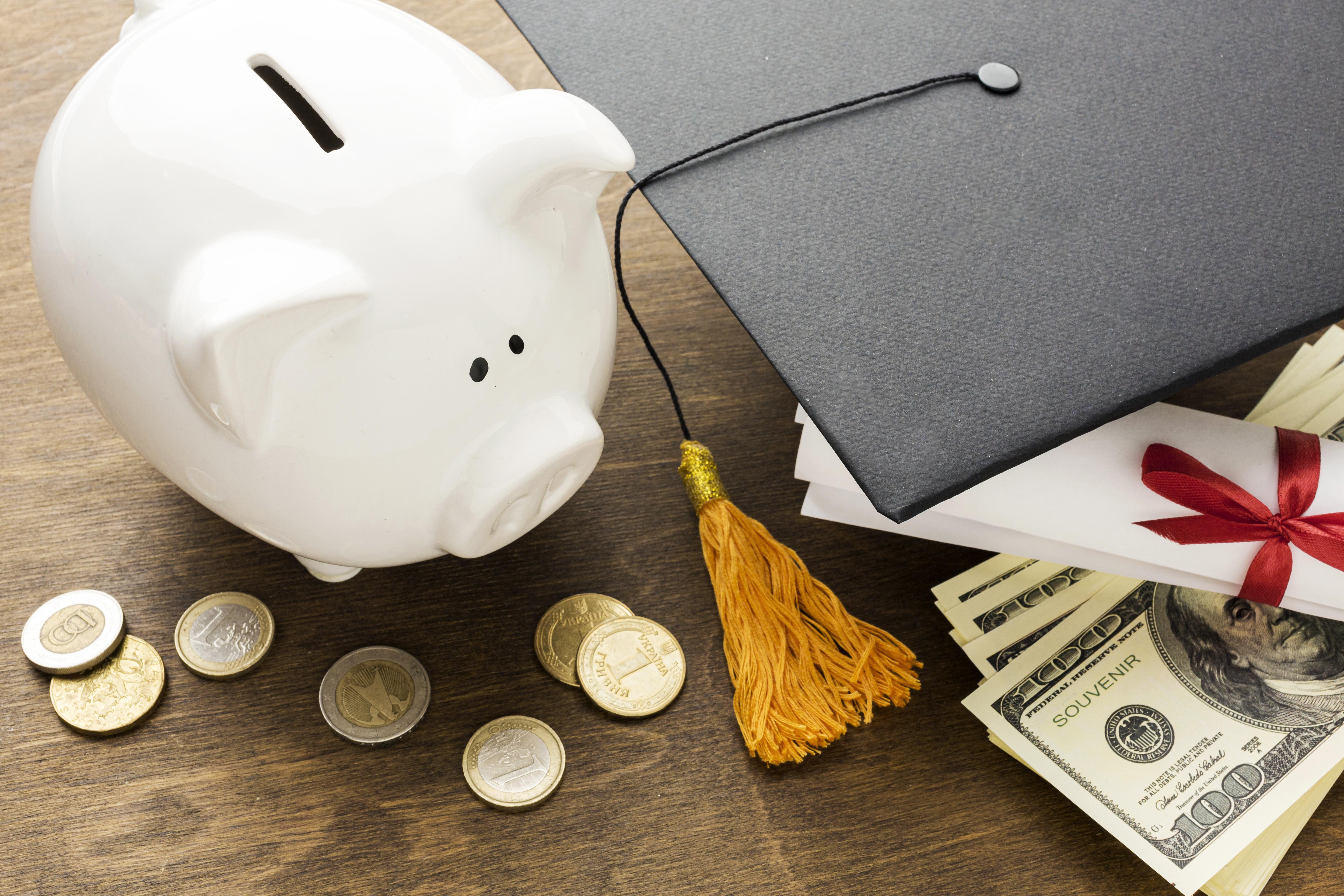 ceramic piggy bank on table with graduation cap, coins, money and diploma